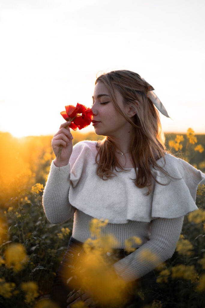 Séance photo portrait dans le Jura : jeune femme tenant une fleur rouge dans un champ fleuri