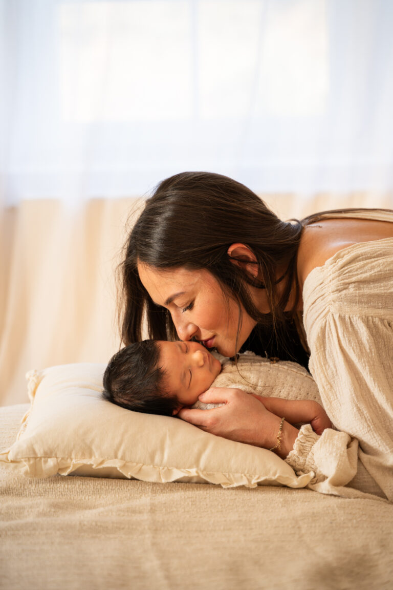 Séance photo naissance en studio à Morez : maman qui embrasse son bébé endormi sur un coussin