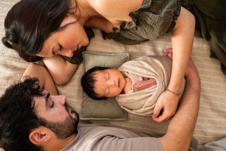 Séance photo naissance en studio à Morez : parents allongés autour de leur nouveau-né emmailloté