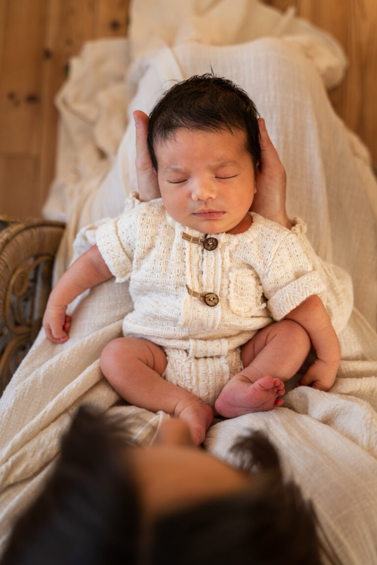 Séance photo naissance en studio à Morez : nouveau-né éveillé en tenue tricotée dans les bras de sa maman