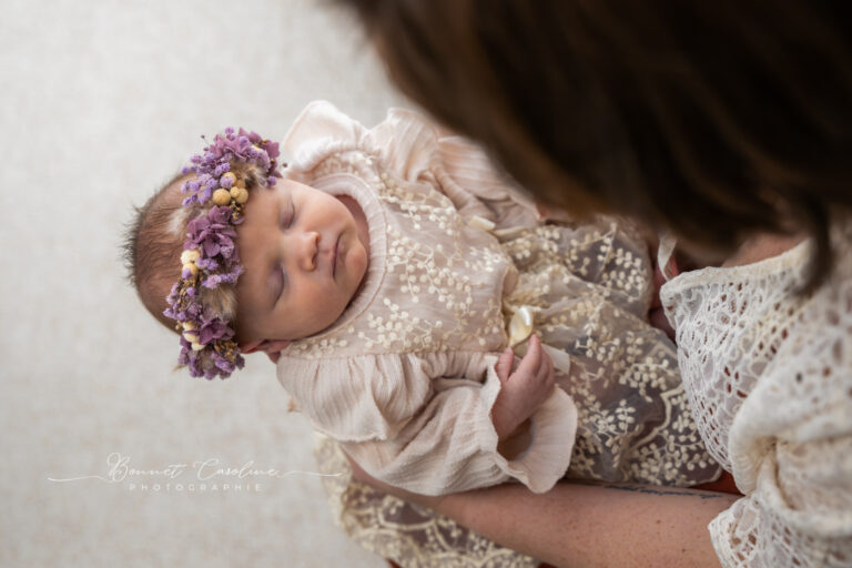 Séance photo naissance en studio à Morez : bébé endormi en dentelle avec couronne de fleurs violettes