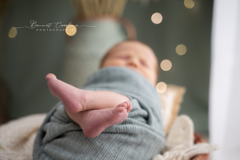 Séance photo naissance en studio à Morez : petits pieds de bébé emmailloté dans un wrap vert