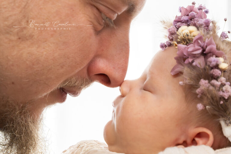 Séance photo naissance en studio à Morez : papa nez contre nez avec son bébé coiffé de fleurs