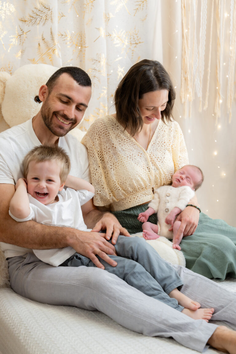 Séance photo naissance en studio à Morez : parents, grand frère et nouveau-né réunis sur le lit