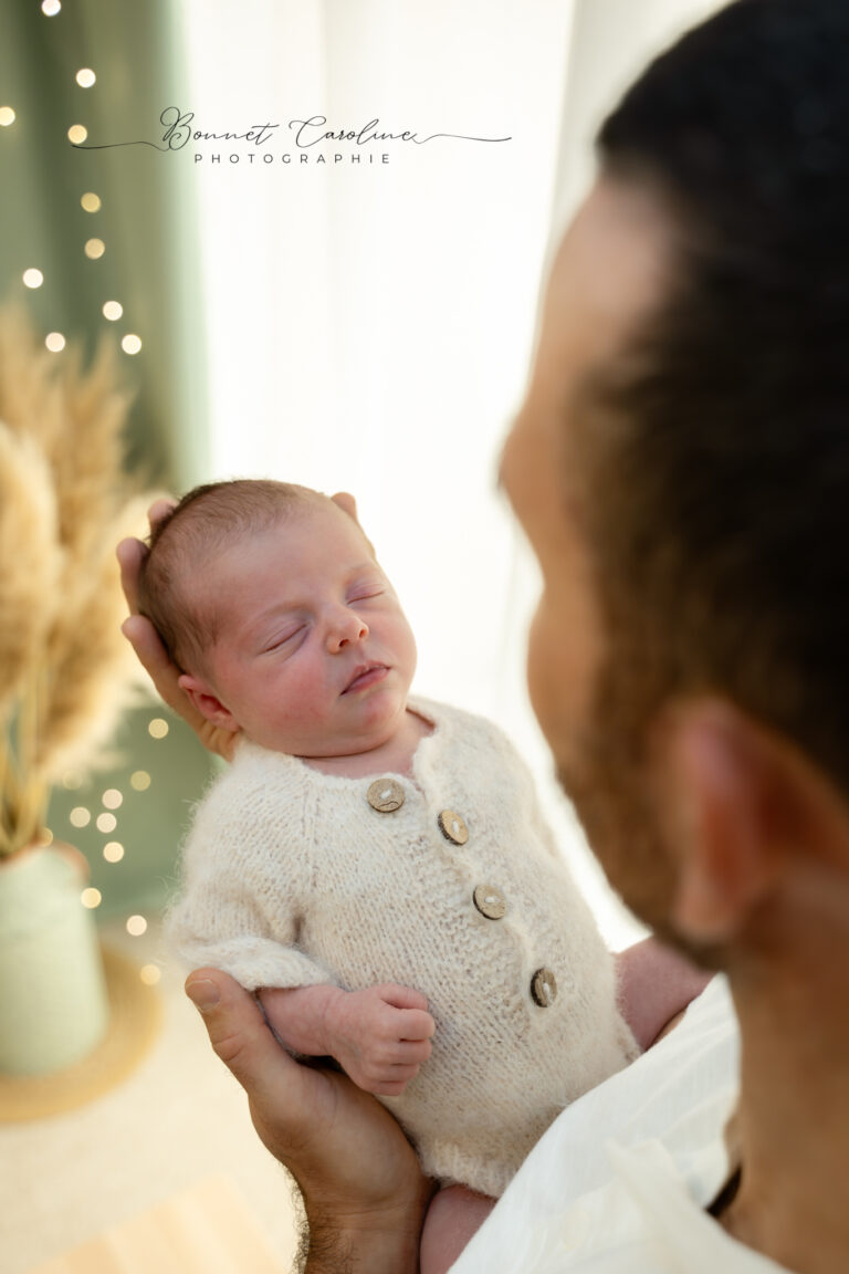 Séance photo naissance en studio à Morez : papa qui tient son bébé en tenue tricotée