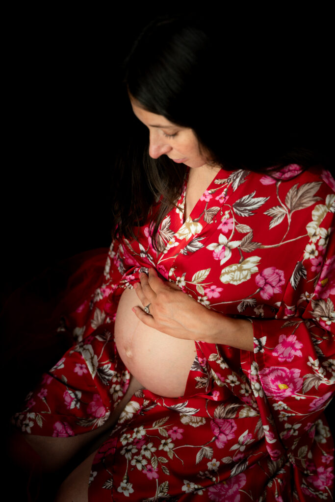 Séance photo grossesse en studio à Morez : future maman en kimono à fleurs rouges sur fond noir