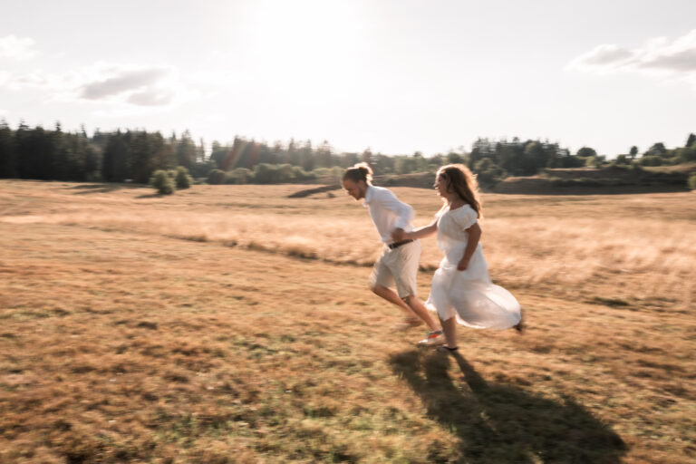 Séance photo couple dans le Jura : couple qui court main dans la main dans un champ en été