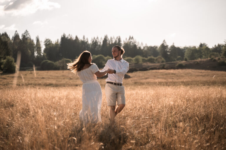 Séance photo couple dans le Jura : couple qui joue dans les herbes hautes face à la forêt