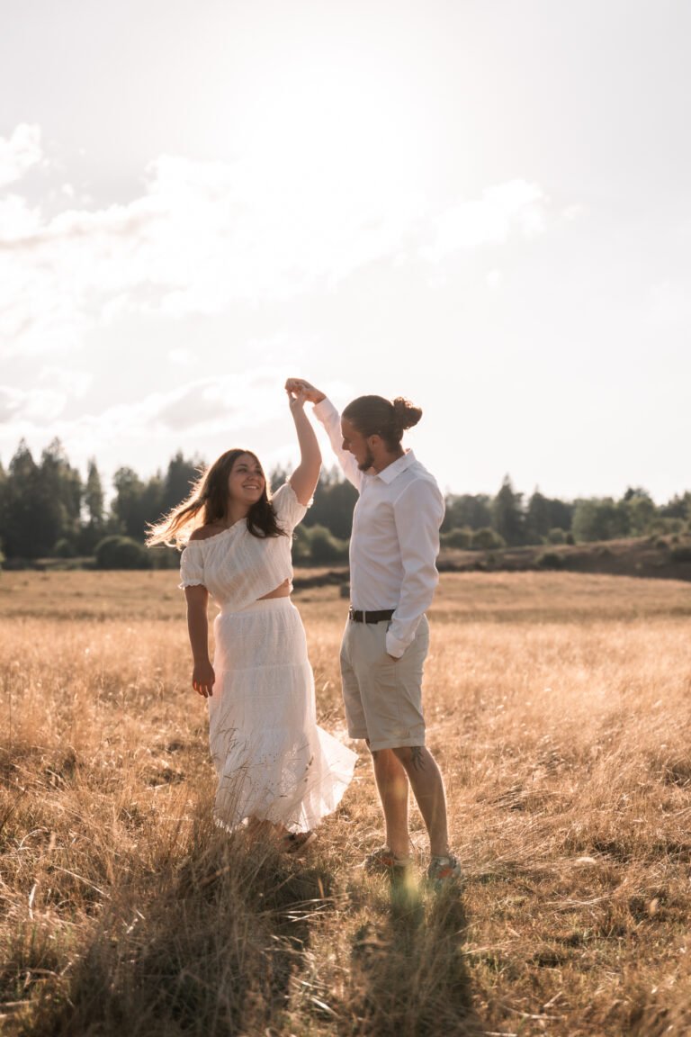 Séance photo couple dans le Jura : couple qui danse dans un champ, bras levés au soleil