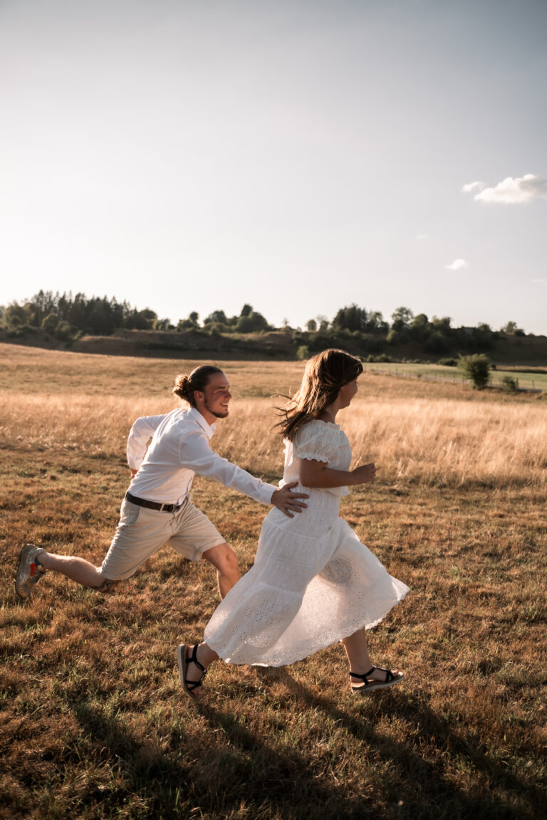 Séance photo couple dans le Jura : couple qui s’élance en courant dans un champ au coucher du soleil