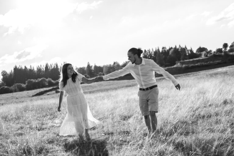 Séance photo couple dans le Jura : couple qui court main dans la main dans un champ, en noir et blanc