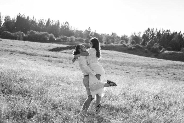 Séance photo couple dans le Jura : homme qui porte sa compagne dans les bras dans un champ, en noir et blanc