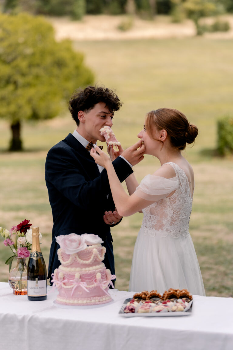 Photographe mariage Jura : mariés qui goûtent leur gâteau de mariage rose