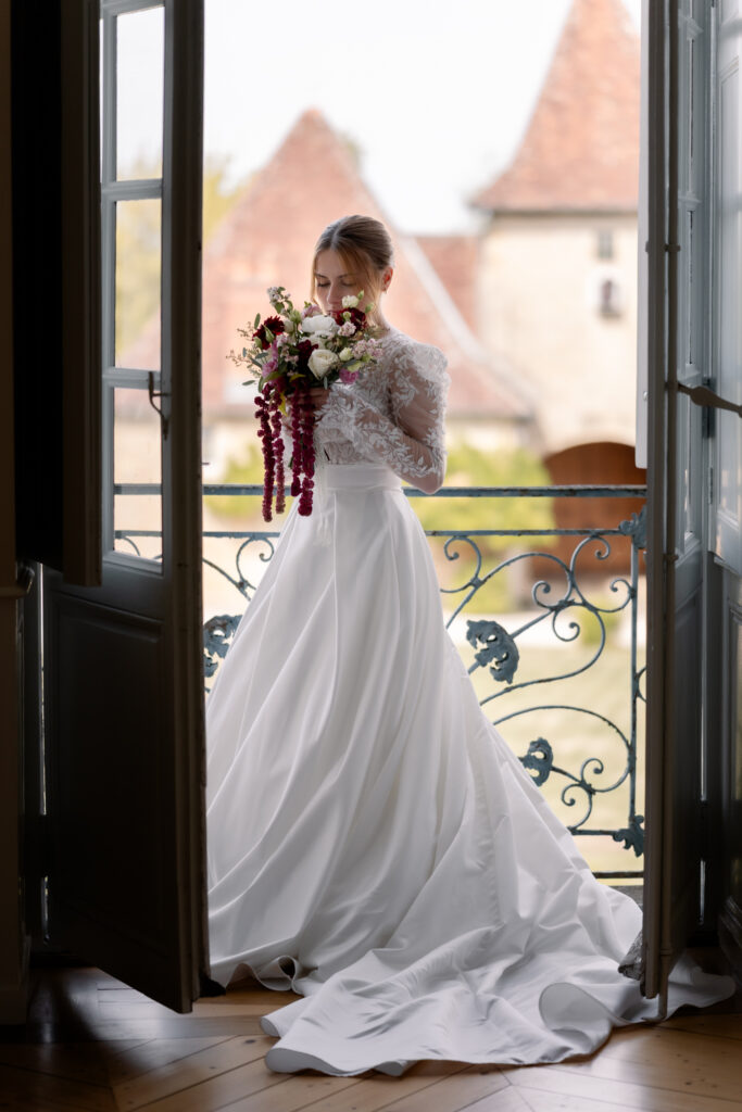 Photographe mariage Jura : mariée qui pose à une porte-fenêtre du château