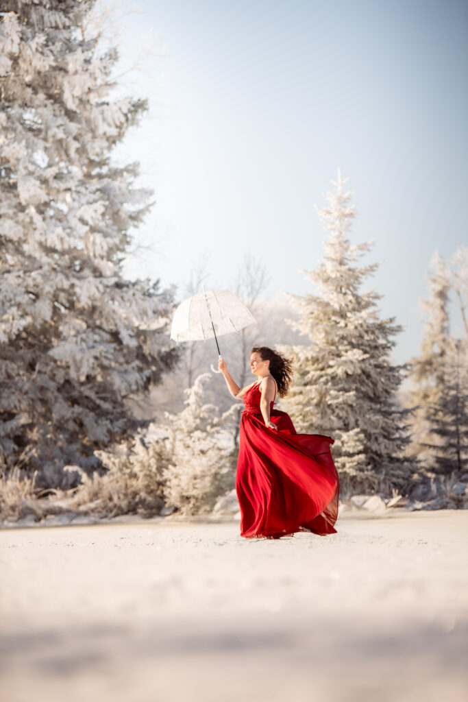 Photographe portrait Morez Jura Genève Lausanne Champagnole Lons-le-Saunier – femme en robe rouge virevoltant entre les sapins enneigés