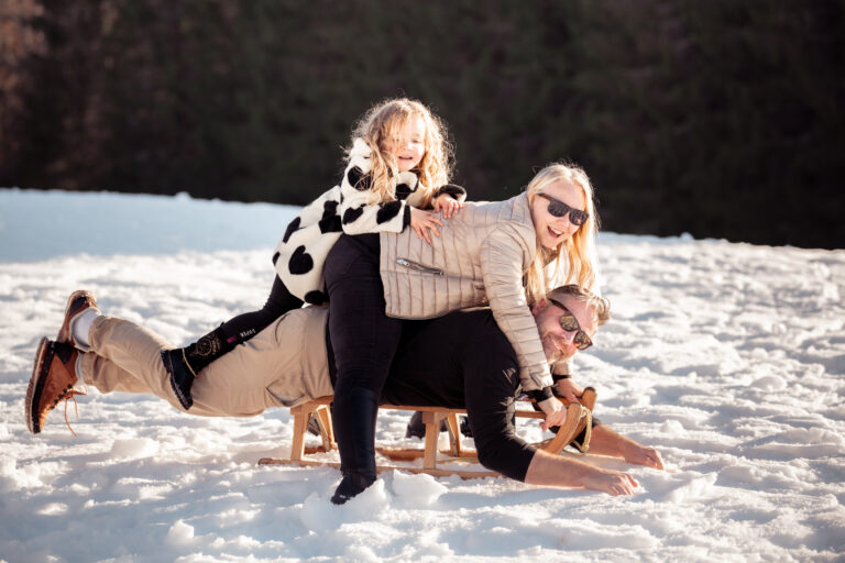 Séance photo famille dans le Haut-Jura : parents et enfant riant sur une luge dans la neige