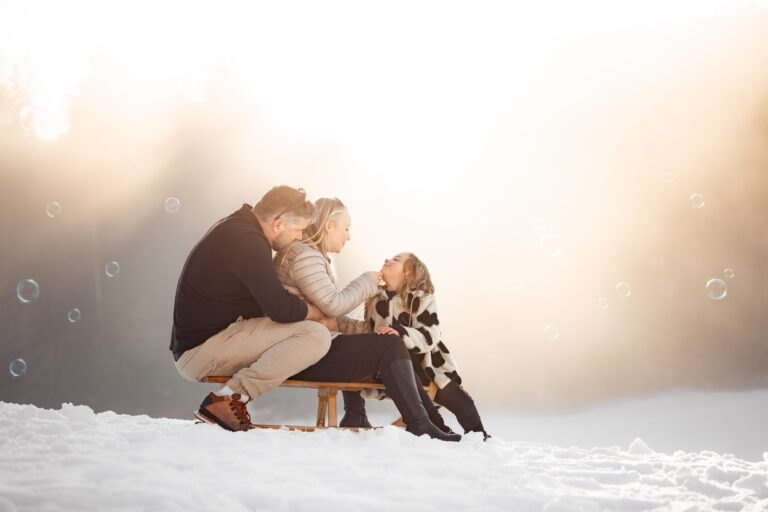 Séance photo famille dans le Haut-Jura : papa et son enfant sur une luge dans la neige au coucher du soleil