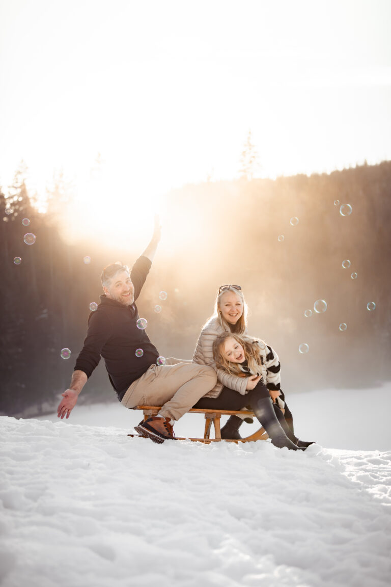 Séance photo famille dans le Haut-Jura : famille autour d’une luge dans la neige à contre-jour