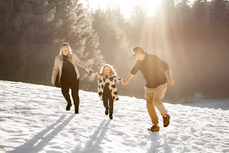 Séance photo famille dans le Haut-Jura : famille courant dans la neige à contre-jour