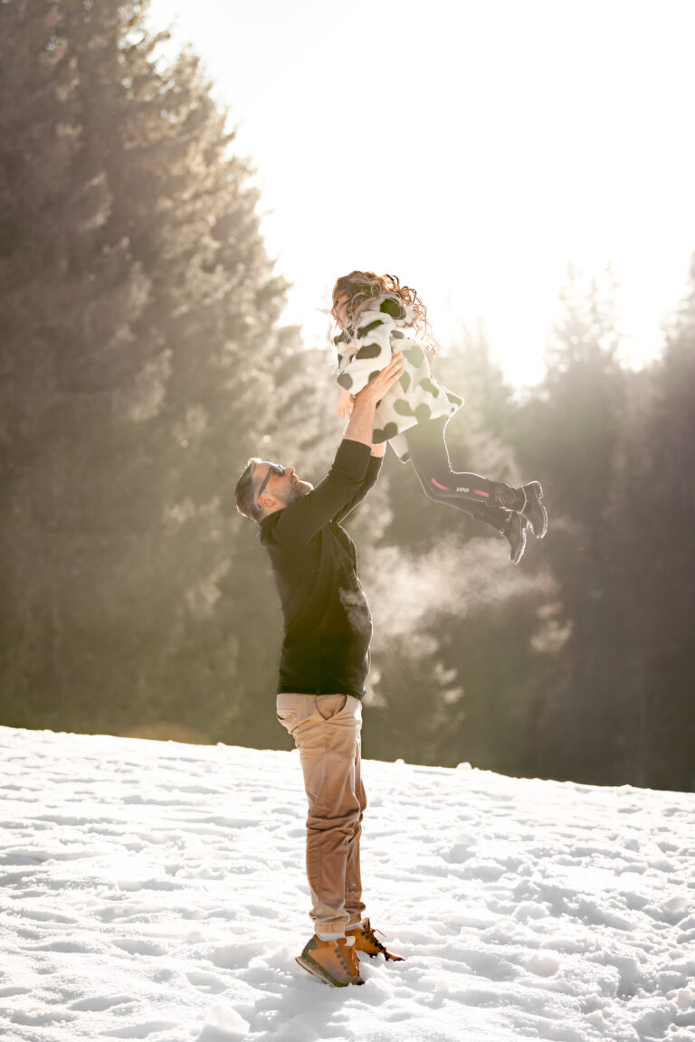 Séance photo famille dans le Haut-Jura : maman lançant son enfant dans les airs dans la neige