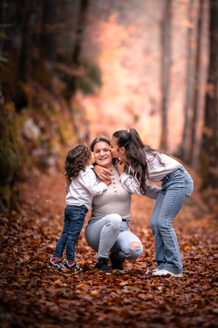 Séance photo famille dans le Haut-Jura : maman jouant avec ses deux filles dans les feuilles d’automne en forêt