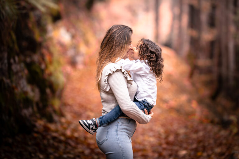 Séance photo famille dans le Haut-Jura : maman portant sa fille dans les bras en forêt d’automne