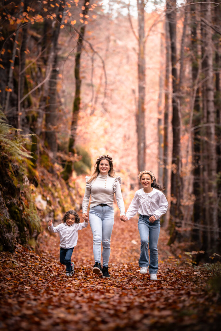 Séance photo famille dans le Haut-Jura : maman et ses deux filles marchant en forêt d’automne