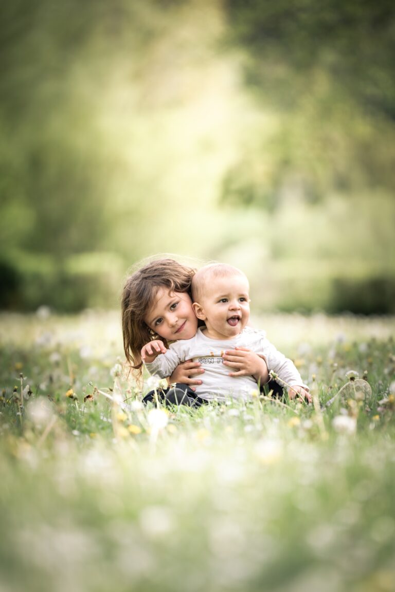 Séance photo famille dans le Haut-Jura : bébé souriant assis dans l’herbe fleurie