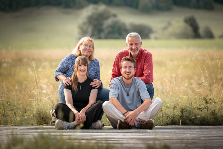 Séance photo famille dans le Haut-Jura : famille assise sur un ponton en bois devant un champ
