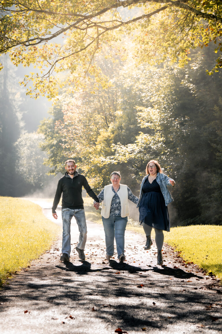 Séance photo famille dans le Haut-Jura : famille marchant main dans la main sur un chemin baigné de lumière