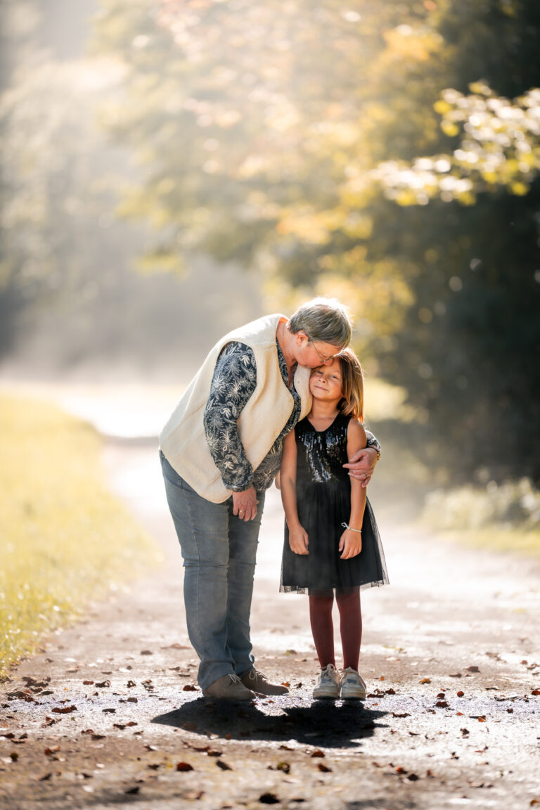 Séance photo famille dans le Haut-Jura : grand-père et sa petite-fille partageant un câlin sur un chemin lumineux