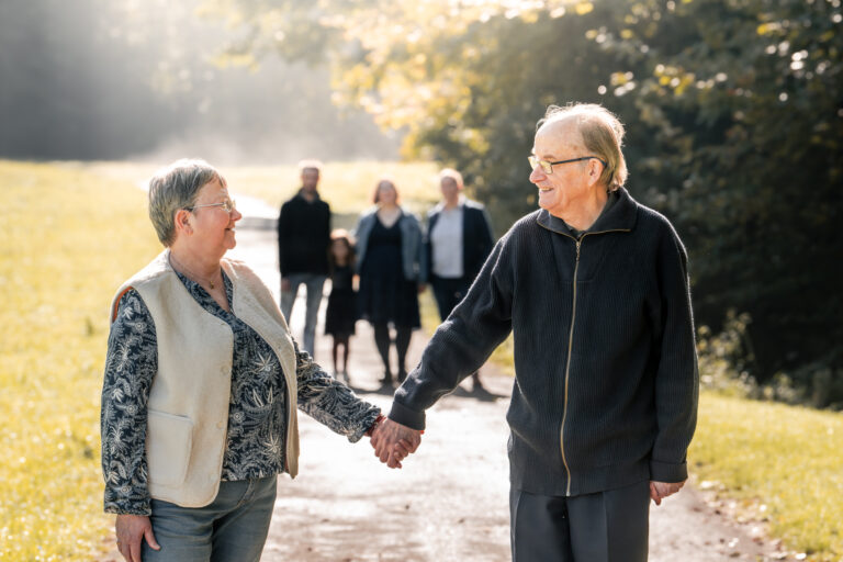 Séance photo famille dans le Haut-Jura : grands-parents main dans la main avec leur famille sur un chemin ensoleillé