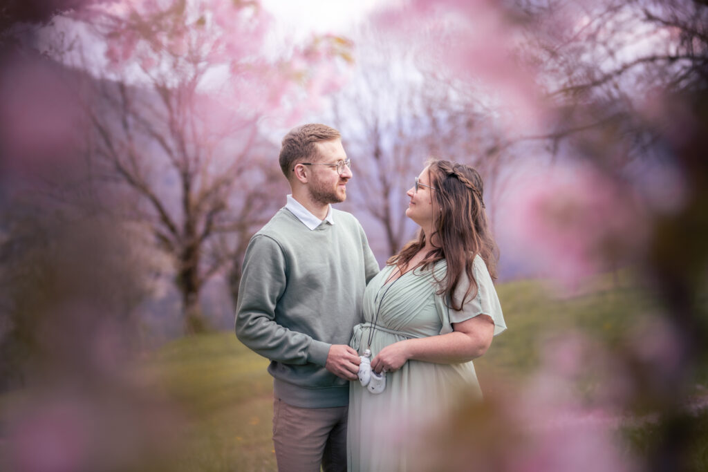 Photographe grossesse Jura – regard complice du couple à travers les fleurs de cerisier