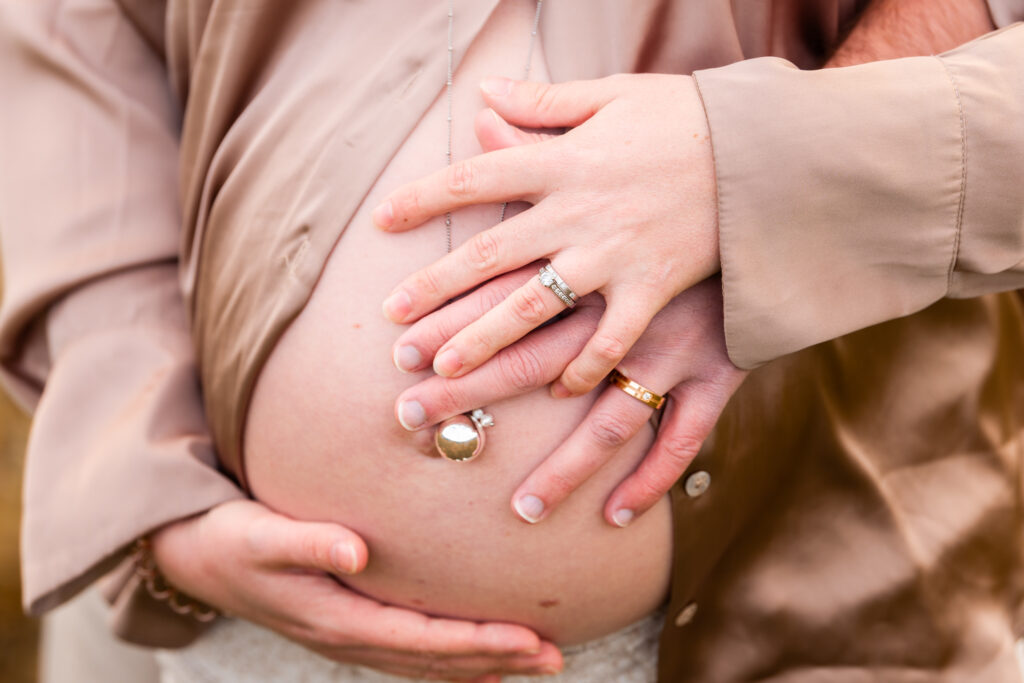 Photographe grossesse Jura – mains des futurs parents posées sur le ventre arrondi