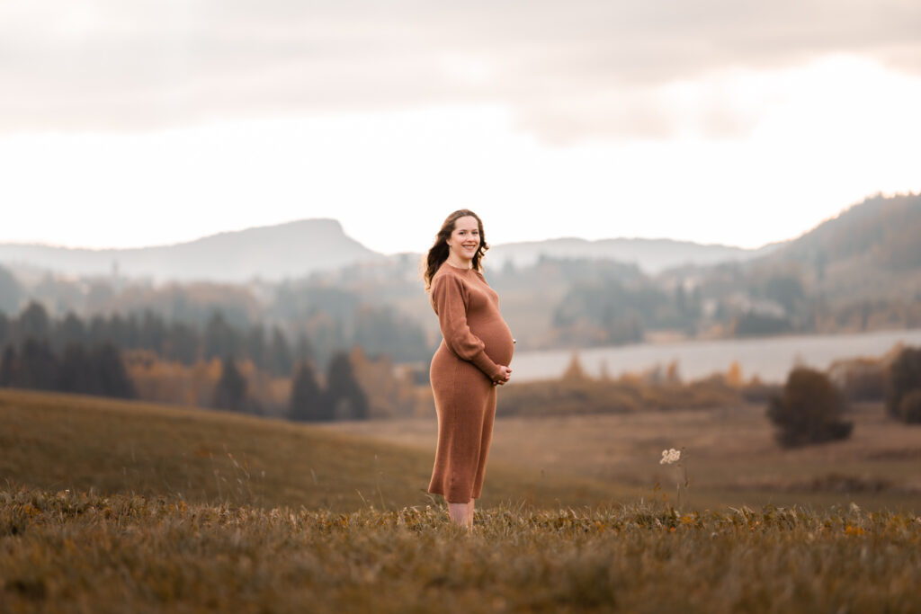Photographe grossesse Jura – future maman dans un champ aux Rousses, vue sur le lac des Rousses et le mont Fier