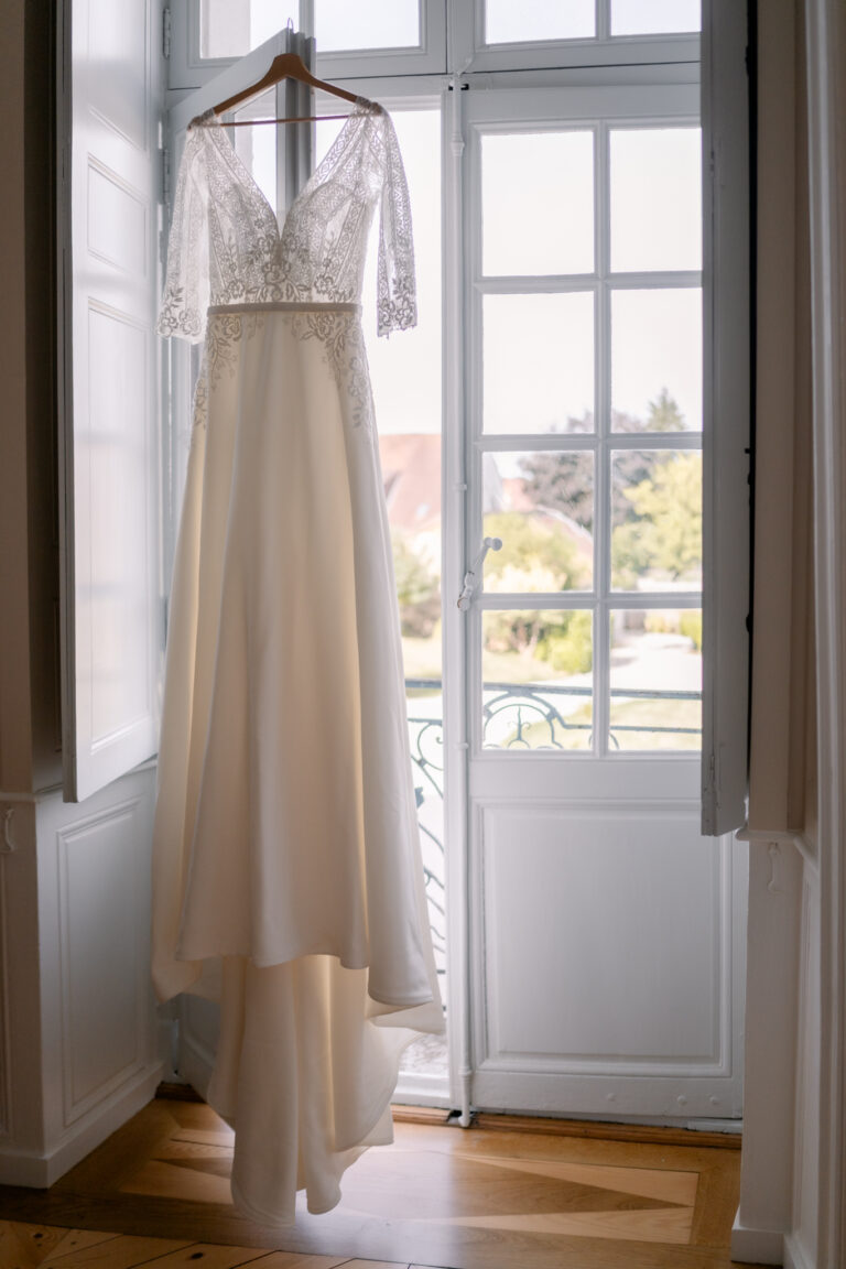 Photographe mariage Jura : robe de mariée suspendue devant une porte-fenêtre