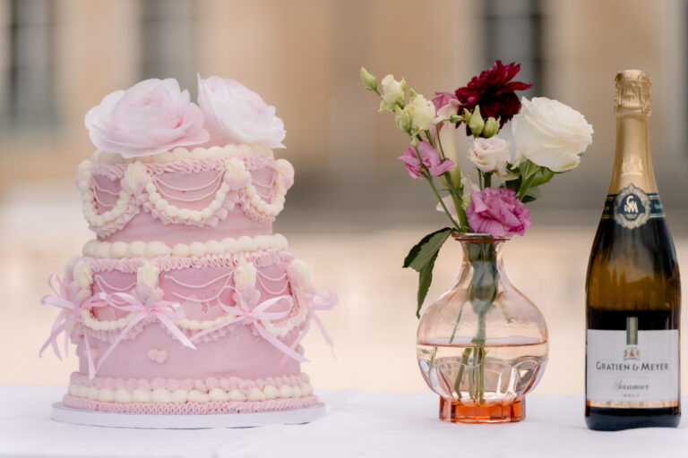 Photographe mariage Jura : gâteau rose à étages, champagne et bouquet de fleurs