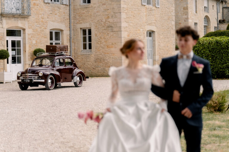 Photographe mariage Jura : mariés qui marchent devant la voiture ancienne