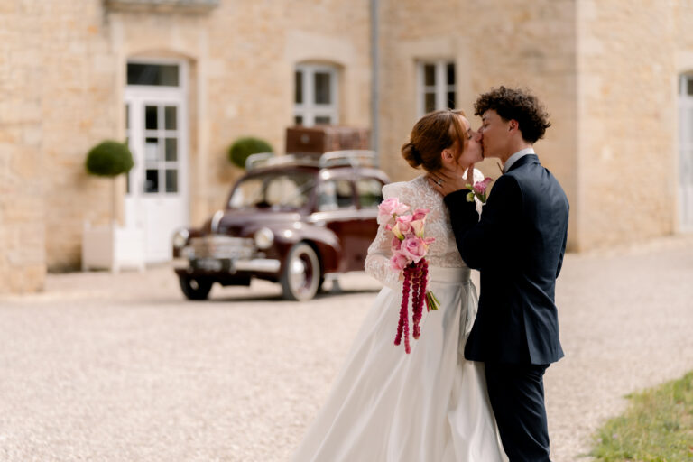 Photographe mariage Jura : mariés enlacés devant la voiture ancienne et la façade du château