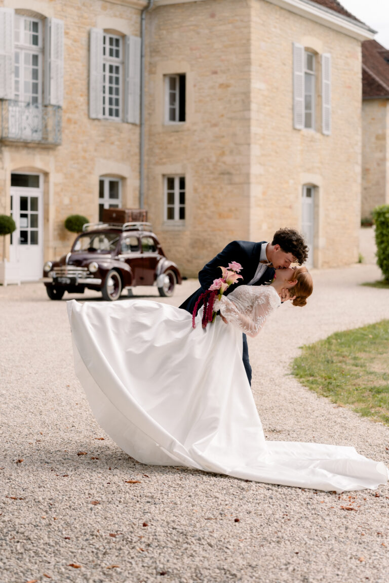 Photographe mariage Jura : marié qui fait basculer sa mariée devant la voiture ancienne