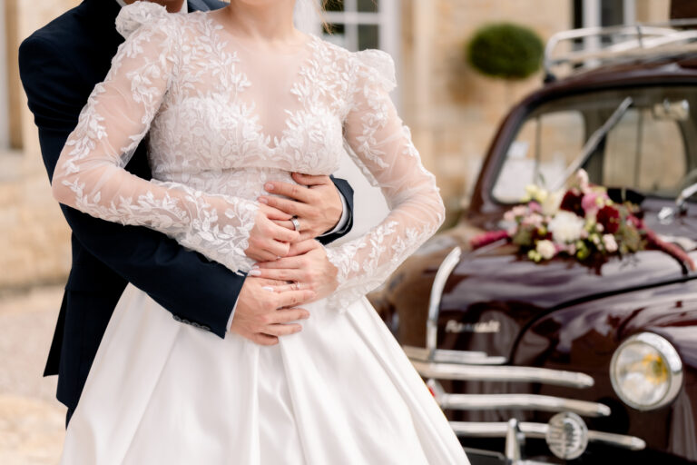 Photographe mariage Jura : marié qui enlace sa mariée devant la voiture ancienne