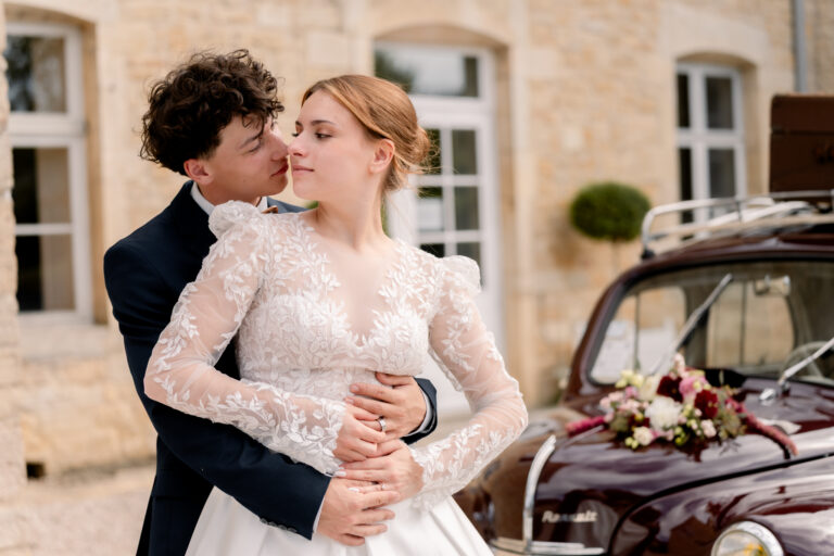 Photographe mariage Jura : marié qui enlace tendrement sa mariée devant la voiture ancienne