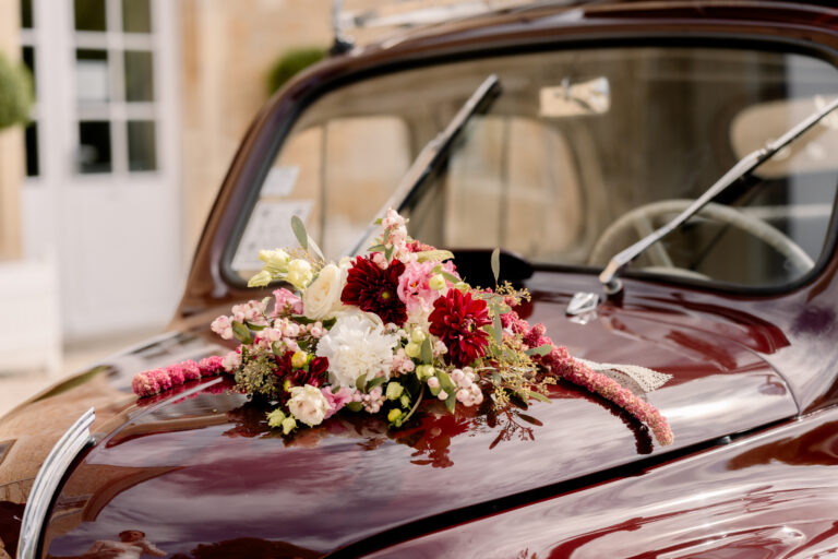 Photographe mariage Jura : fleurs roses et bordeaux sur le capot de la voiture ancienne