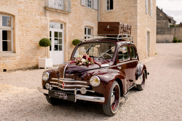 Photographe mariage Jura : voiture ancienne bordeaux avec valise sur le toit, devant le château