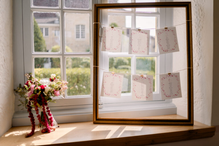 Photographe mariage Jura : plan de table sur une fenêtre ancienne fleurie