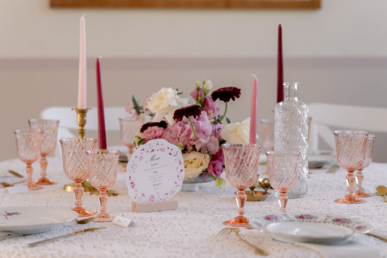 Photographe mariage Jura : chandeliers dorés, verres roses et menu sur la table