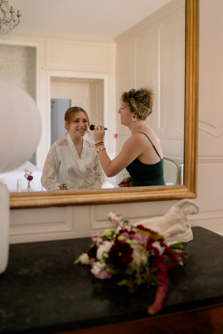 Photographe mariage Jura : mariée qui se fait maquiller devant le miroir