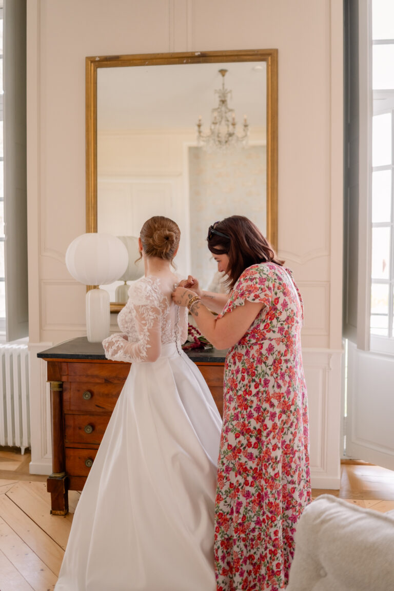 Photographe mariage Jura : mariée aidée pour fermer sa robe