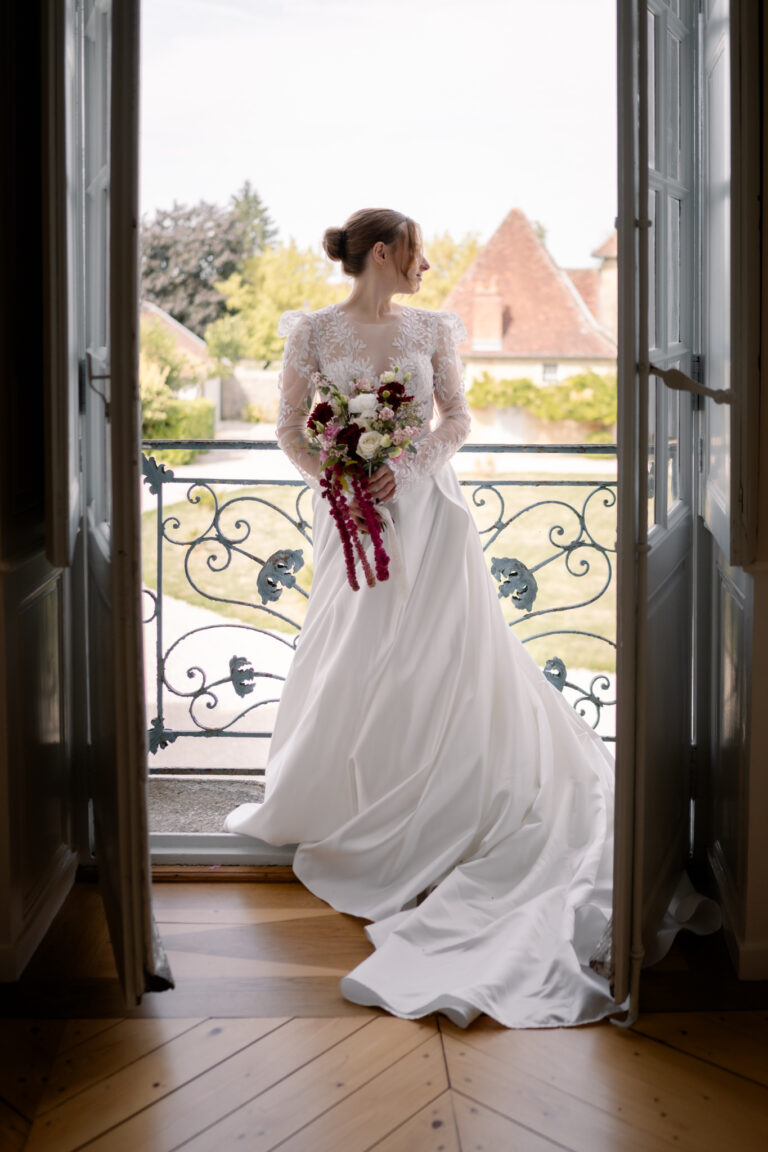 Photographe mariage Jura : mariée à la porte-fenêtre du balcon