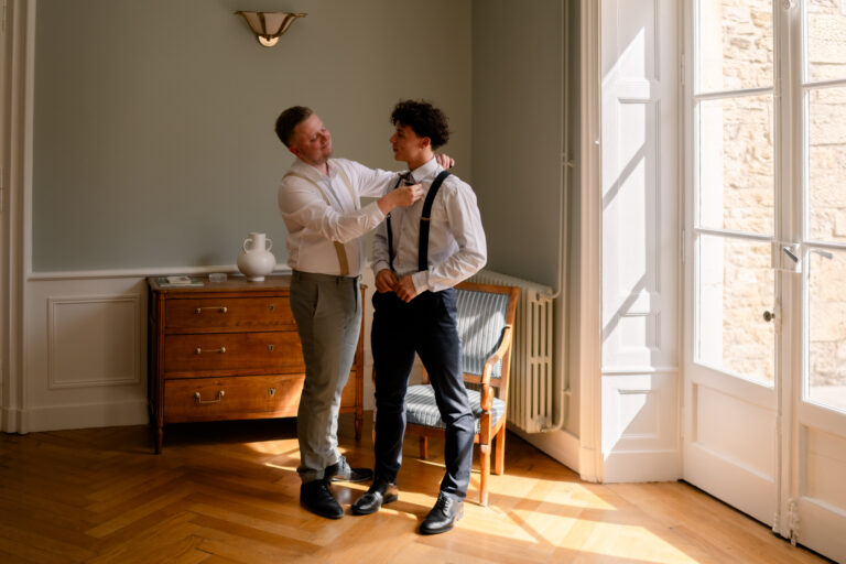 Photographe mariage Jura : marié aidé par un proche pour ses bretelles